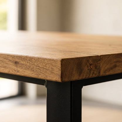 Acacia plank grain and squared edge of the six-seat dining table top above the black iron leg (close-up detail)