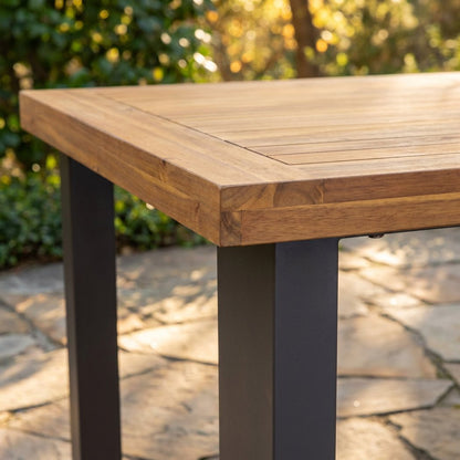 Square matte-black iron leg meeting the framed acacia plank top at the corner of the six-seat dining table (close-up detail)