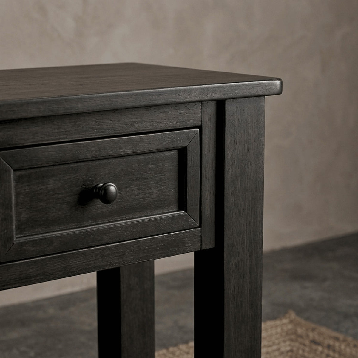 A drawer and leg of the table above a jute rug in soft side light