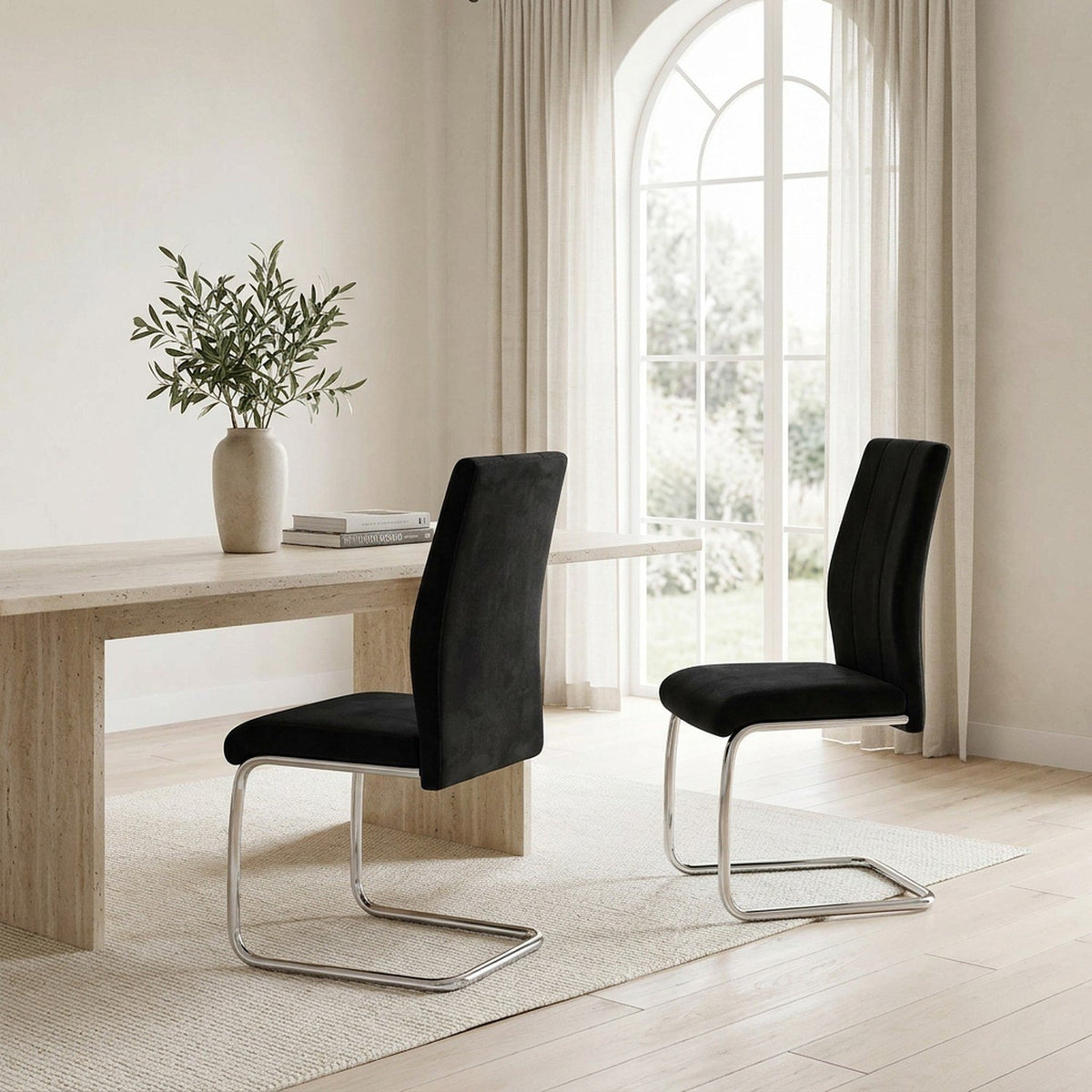 Black velvet chairs at a dining table beside an arched window, wide view