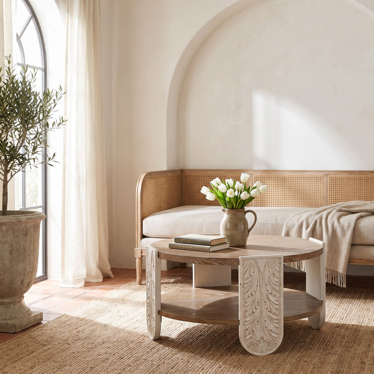 Low window-side view of the round carved wood coffee table in the same whitewashed room