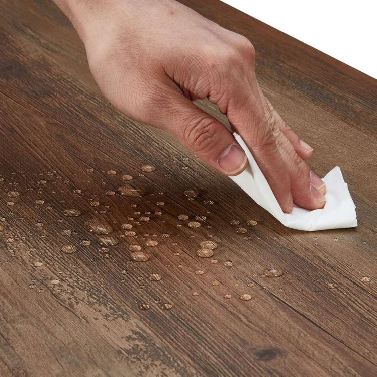 Hand wiping water droplets from a rustic wood finish surface, part of a mid-century TV stand with storage.