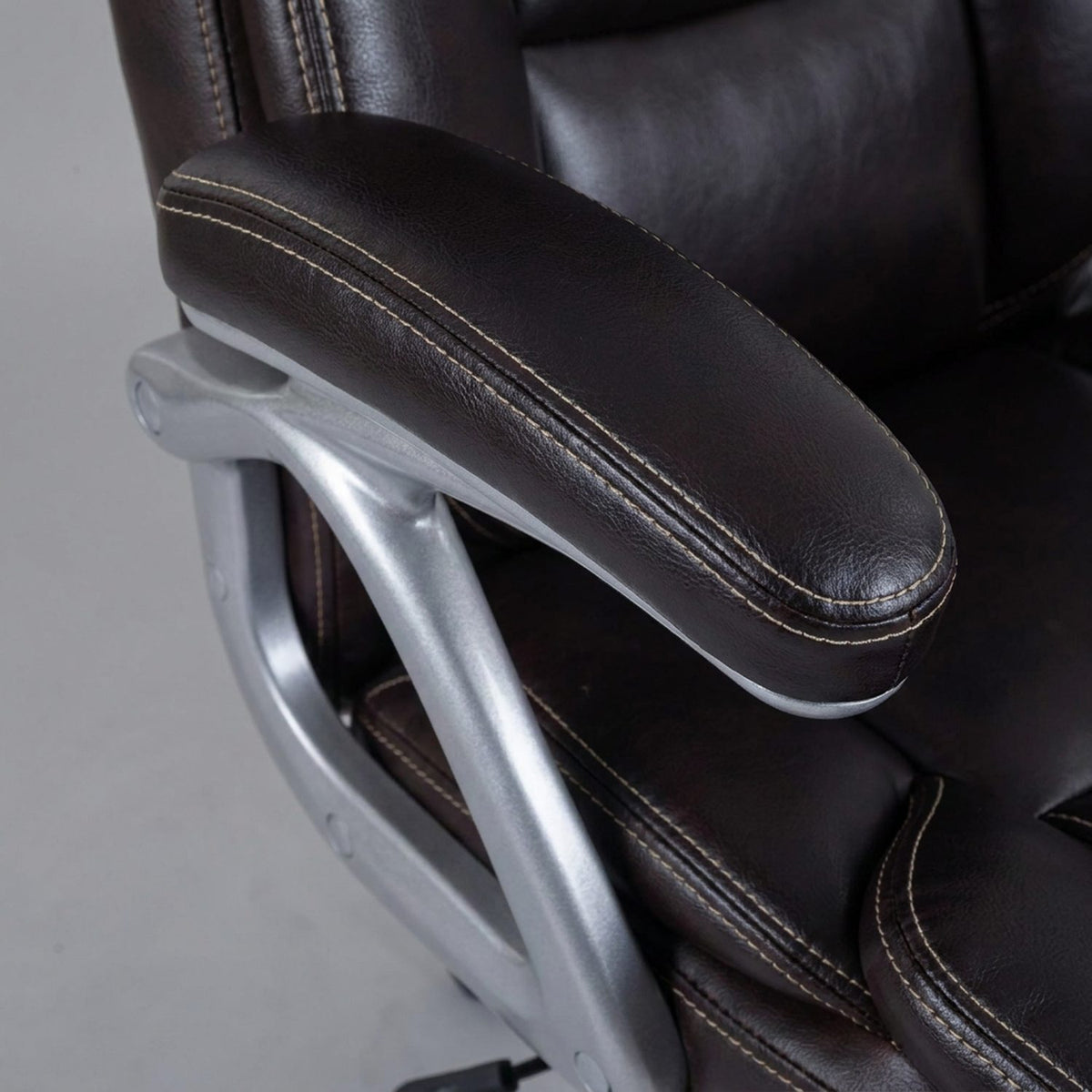 Close-up of the padded armrest on its silver arm frame beside the waterfall seat edge (close-up detail)