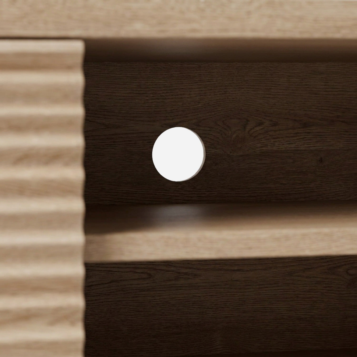 Round cable hole in the dark back panel of the open bay, shelf edge below (close-up detail)