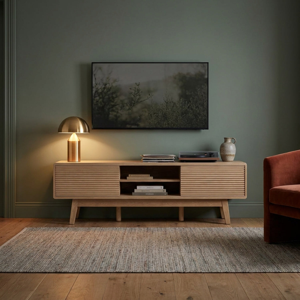 Oak media console with fluted doors in a sage-green living room at dusk, brass lamp and turntable on top