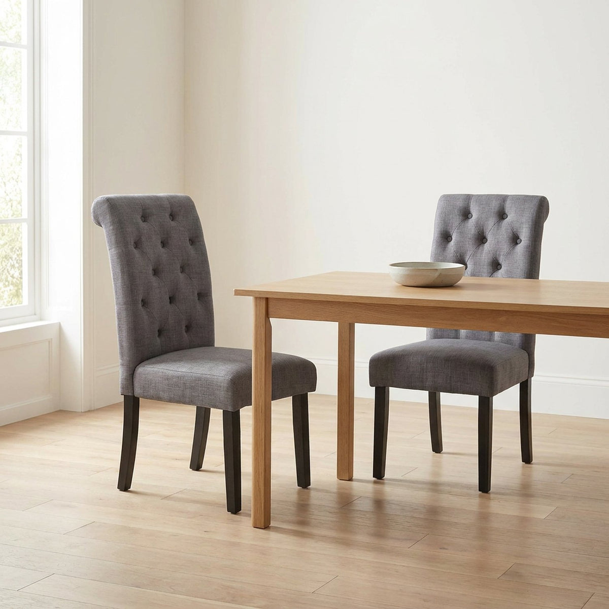 Two gray tufted dining chairs at a light oak table in a bright dining room
