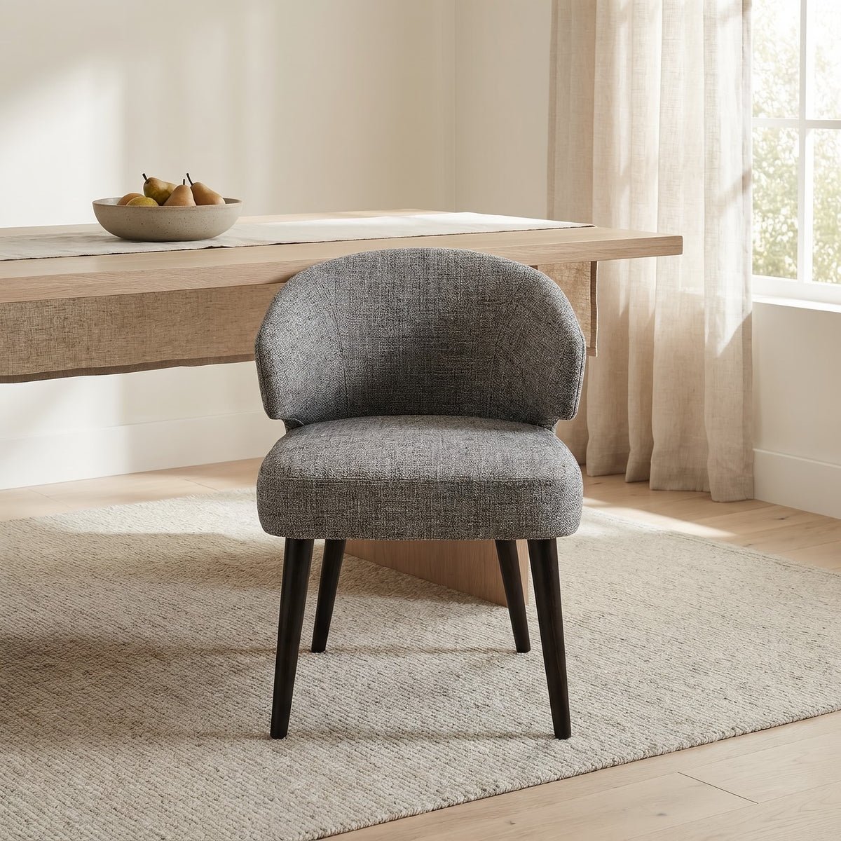 Grey fabric dining chair at the end of a pale oak table in a sunlit dining room, closer view (room scene)