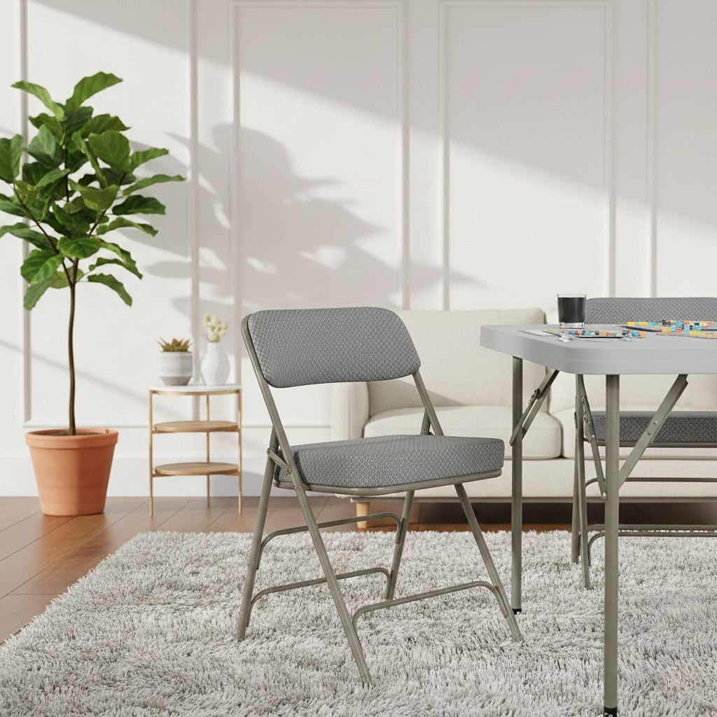 2-pack Hercules folding chairs with gray cushioned fabric seats and metal frames by a table in a bright living room.