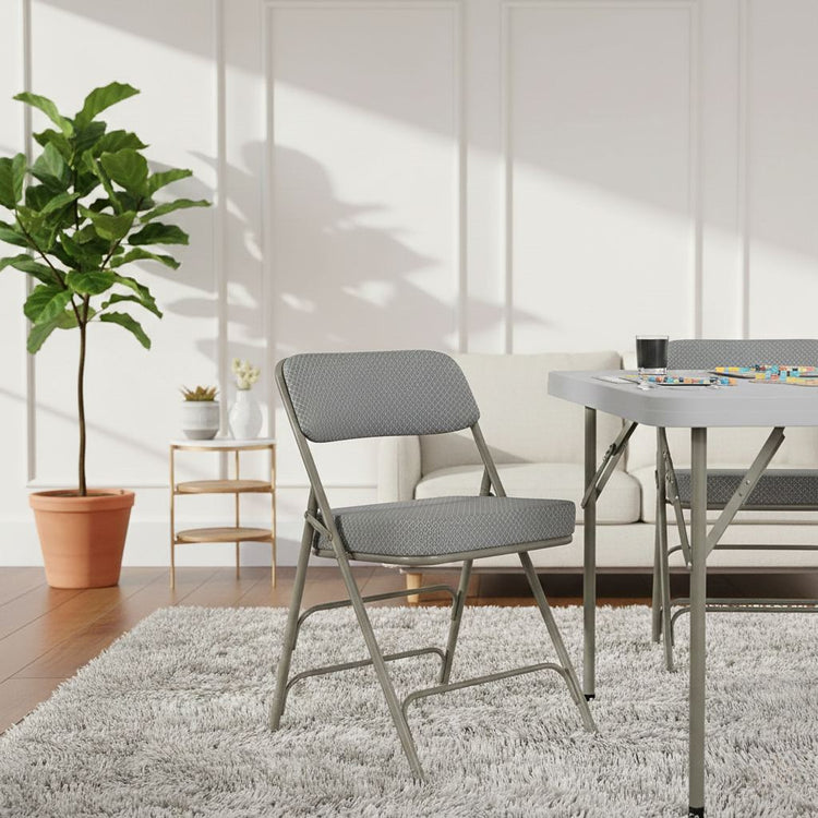 2-pack Hercules folding chairs with gray cushioned fabric seats and metal frames by a table in a bright living room.