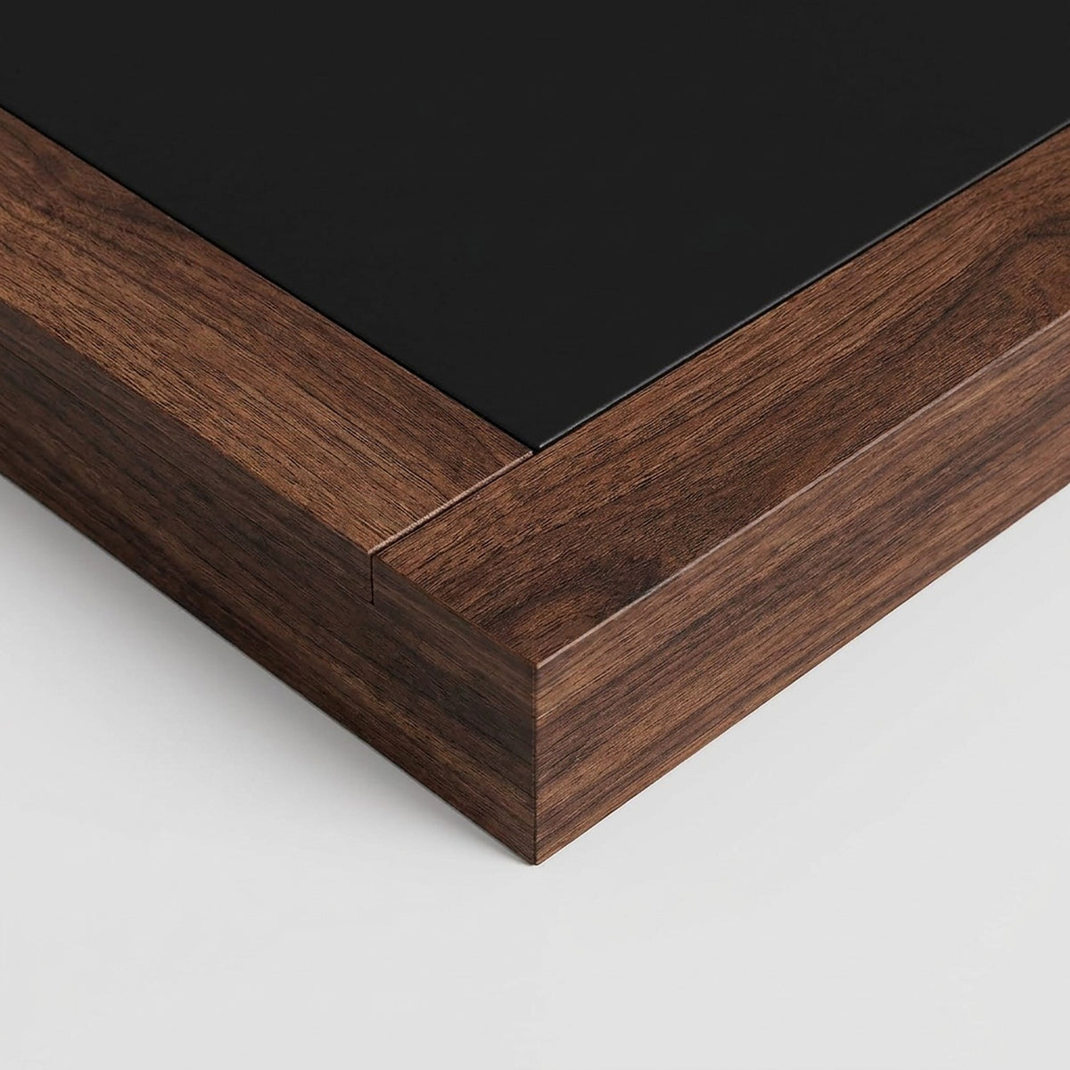 Close-up of the walnut desktop frame meeting the black inset at a thick corner edge