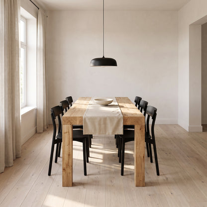 Light oak extendable dining table at full length under a black pendant in a white plaster dining room