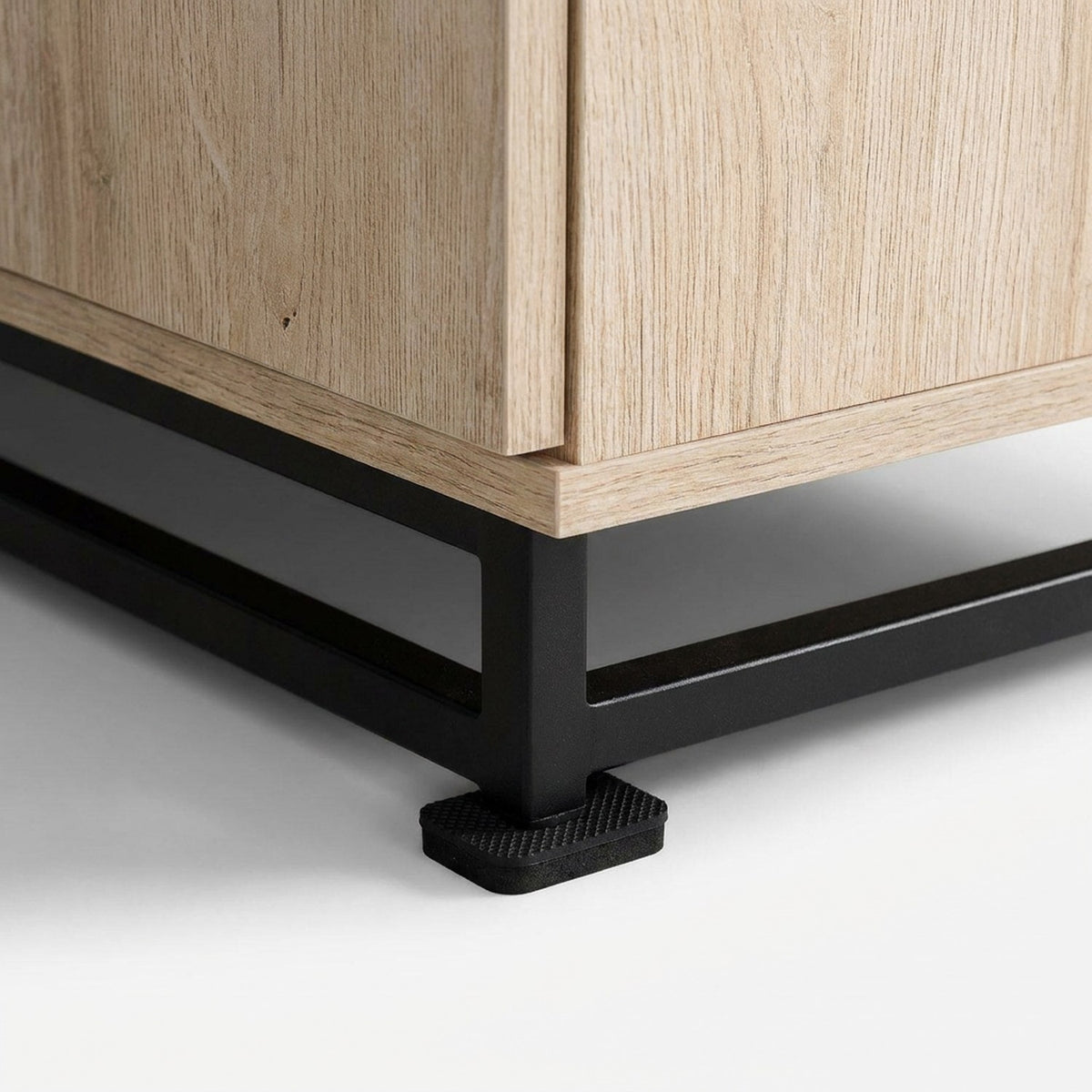 Black steel sled foot with rubber pad under an oak-grain door corner, close-up detail