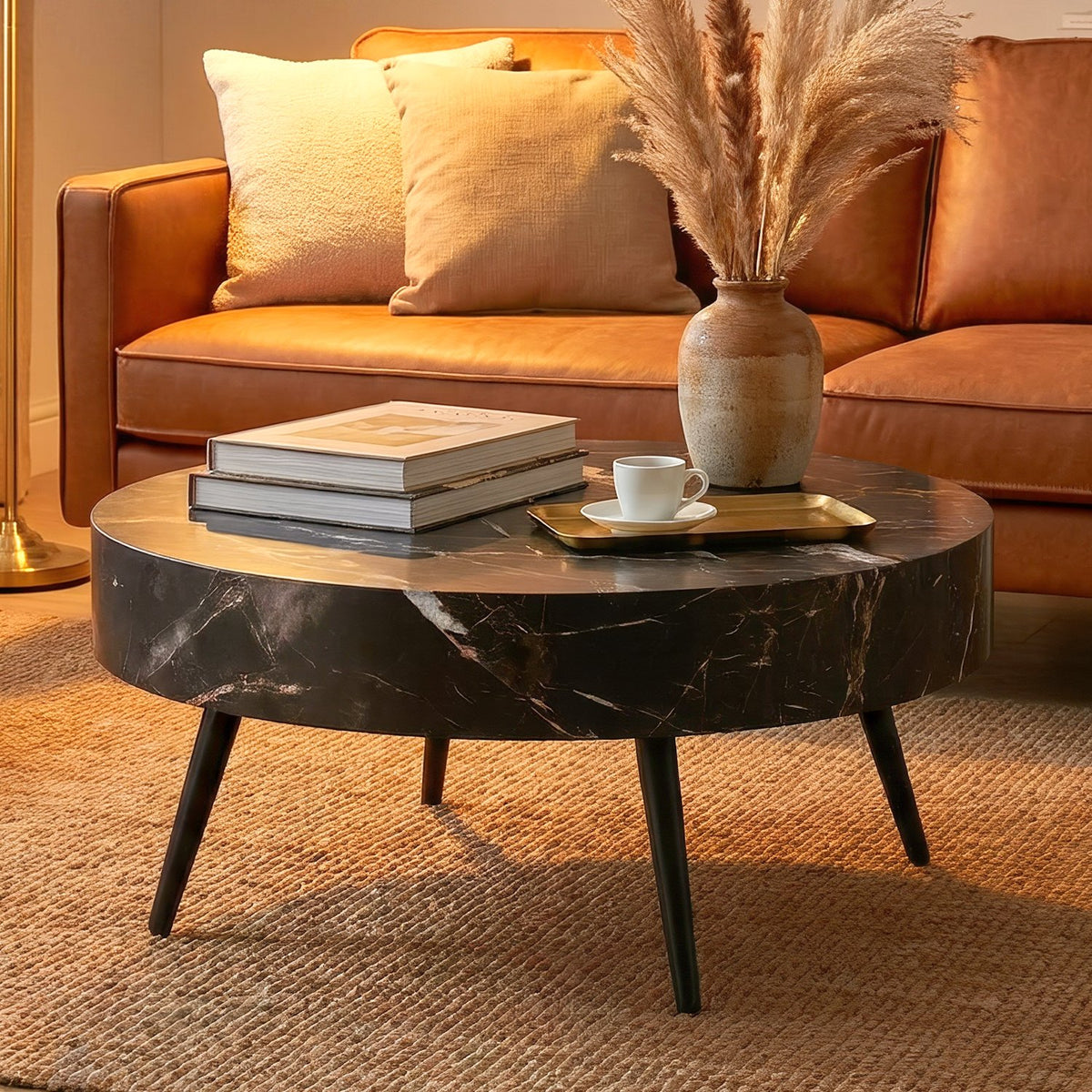 Closer view of the black marble table with art books, a brass tray and a pampas vase beside a cognac sofa