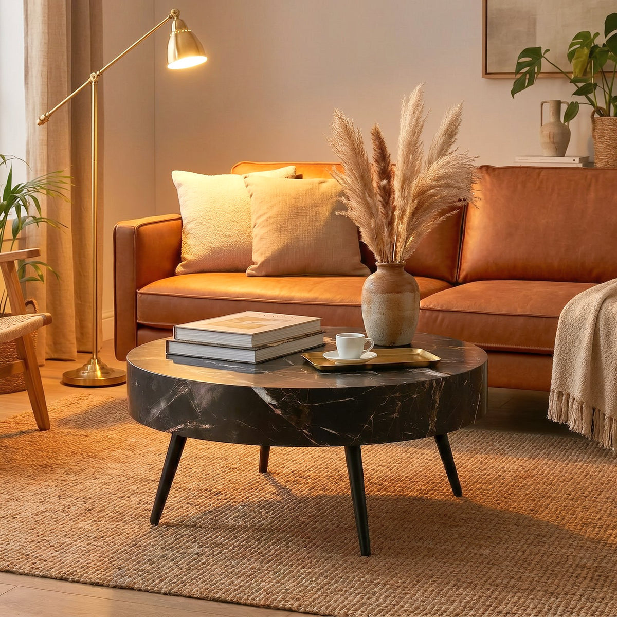 Black marble round table on a jute rug before a cognac leather sofa in a lamplit living room