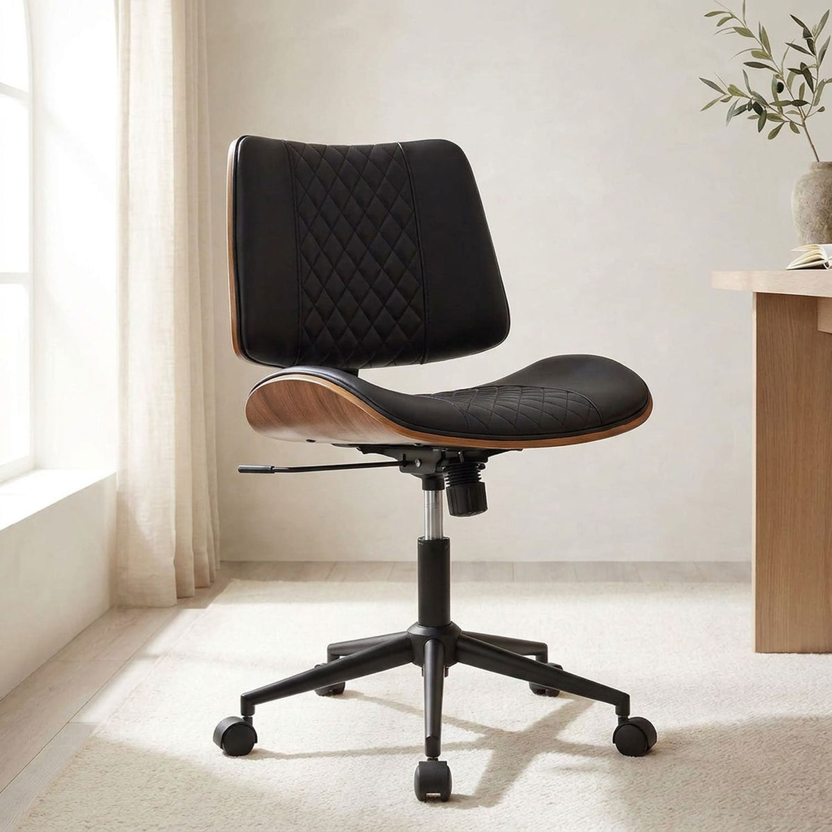 Black ergonomic office chair in three-quarter view beside a wooden desk in a limewash room