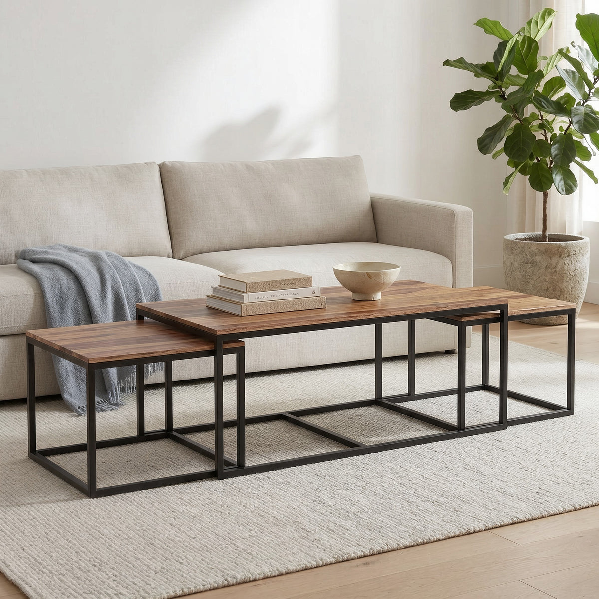 Sheesham wood nesting tables in front of a linen sofa with a gray throw, stacked books and a bowl in a sunny living room
