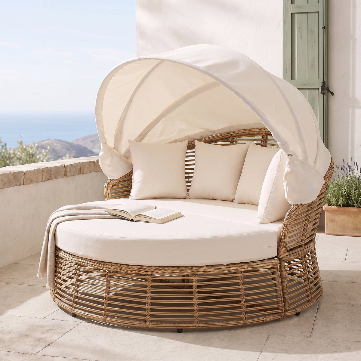 Wicker daybed with a folded throw and open book, seen from the opposite side