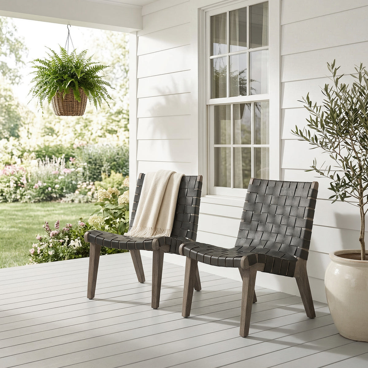 Pair of outdoor lounge chairs on a white porch beside an olive tree and hanging fern