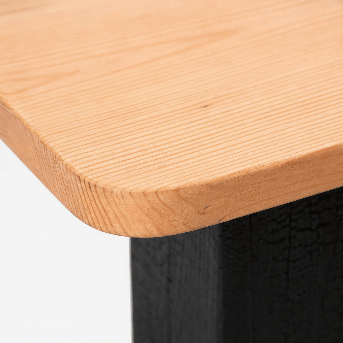 Rounded corner and straight grain of the natural reclaimed wood top, on a light grey ground (close-up detail)