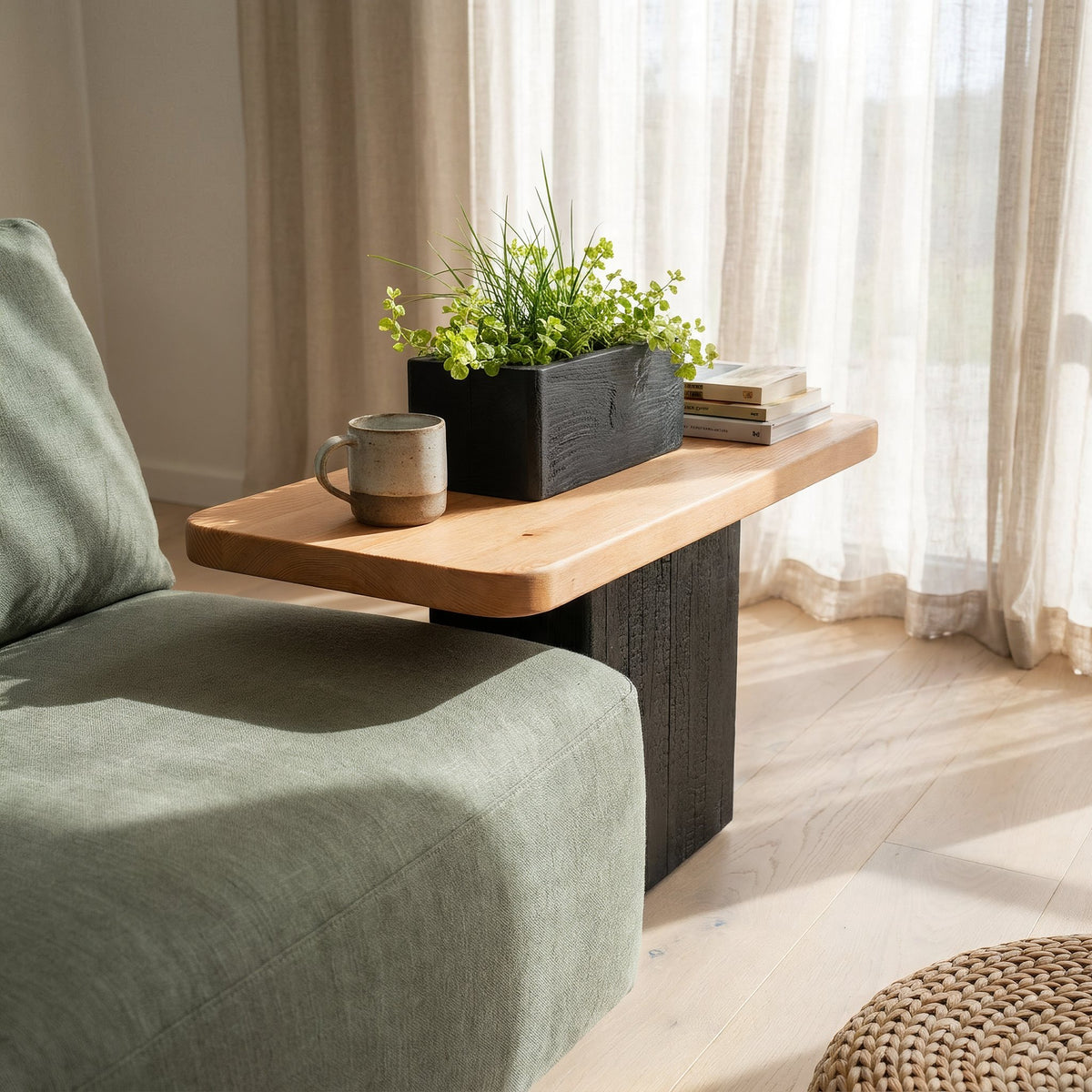 Planter side table holding a mug, books and trailing greenery by a sage sofa in a bright sunroom