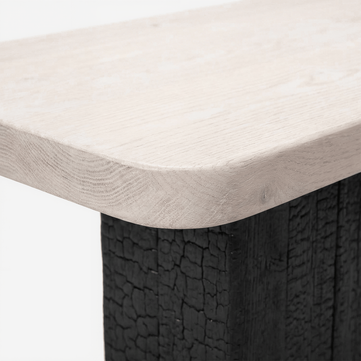 Rounded corner of the white-stained wood top over the torched black base, on a light grey ground (close-up detail)