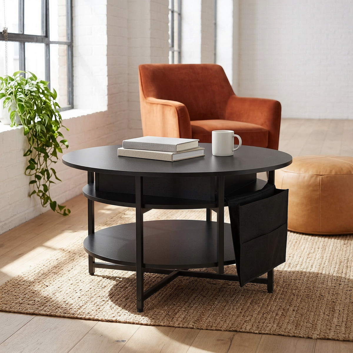 Round black lift-top coffee table with a side pocket on a jute rug in a sunlit loft by a brick wall and window, with books and a mug on top
