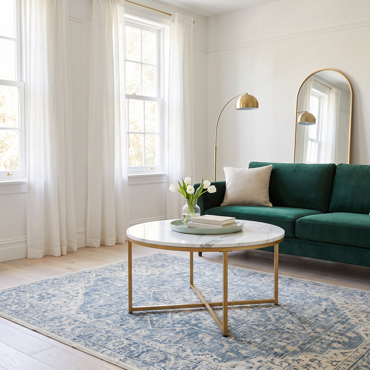 Round white faux-marble coffee table with gold base in front of a green sofa in a bright living room