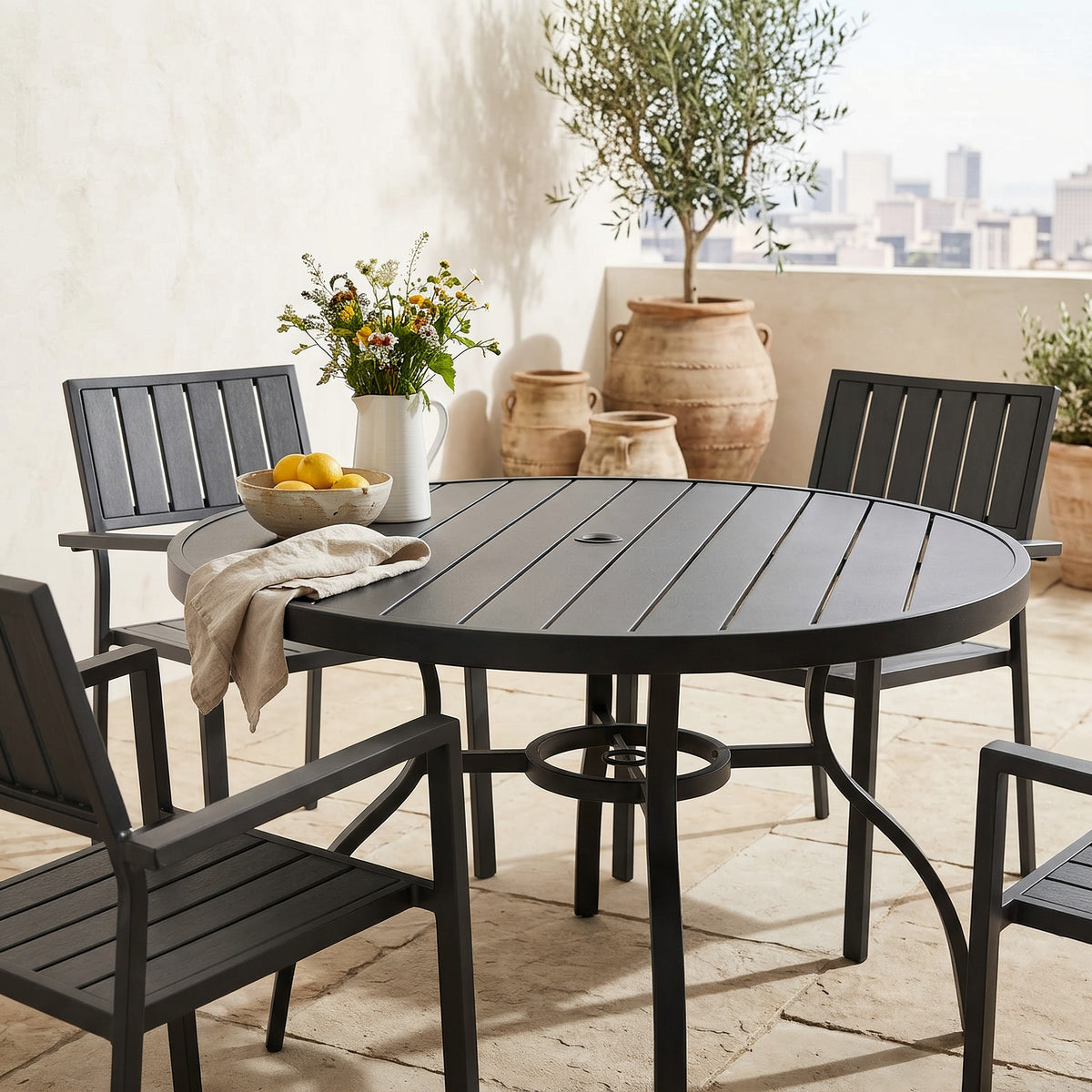 Close view of the black round outdoor dining table and armchairs on a terrace beside a warm plaster wall with clay pots