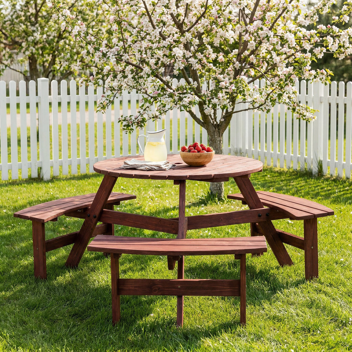 Fir wood circular picnic set with three benches on a spring lawn under an apple blossom tree beside a white picket fence