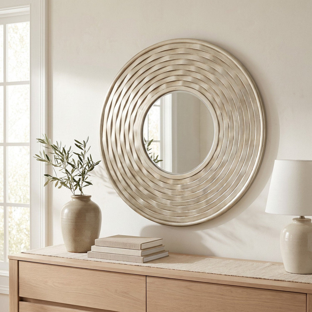Round silver sculpted wall mirror hung above an oak dresser in a bright bedroom