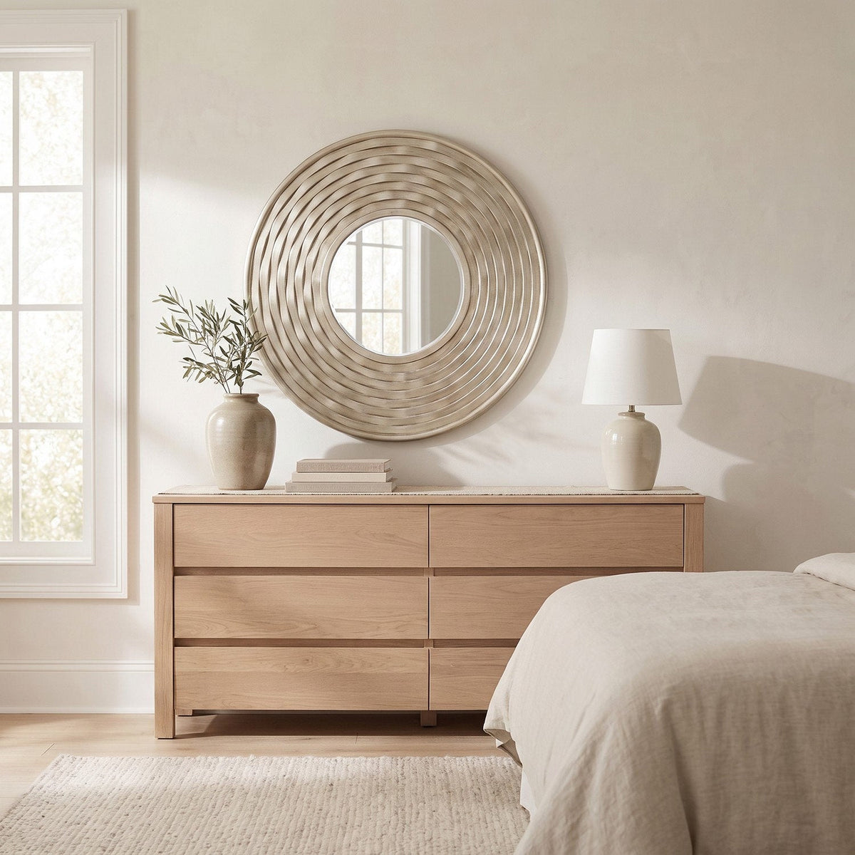 Wider view of the bedroom with the round silver wall mirror above the dresser