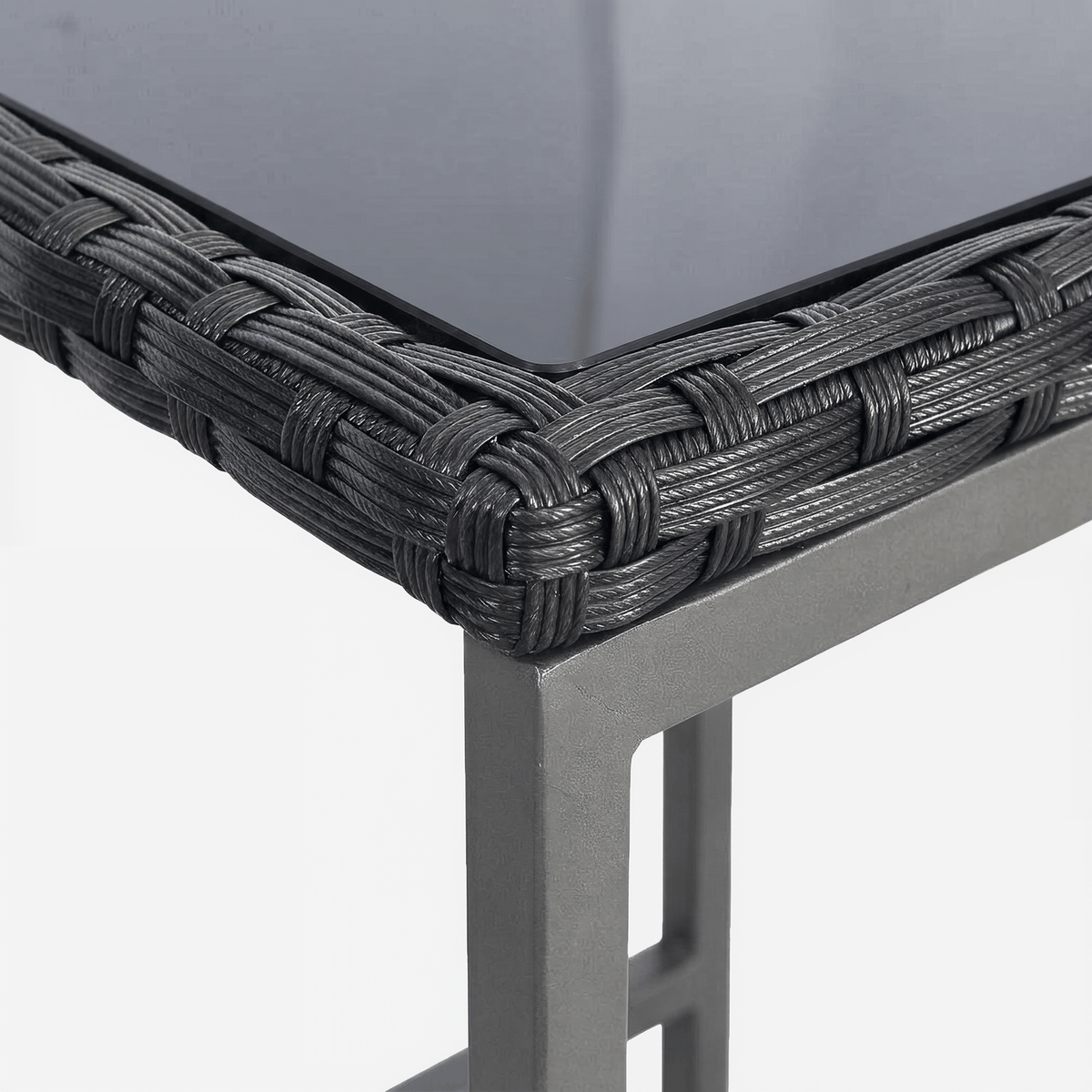 Wicker-wrapped corner of a dark glass tabletop above a square steel leg (close-up detail)