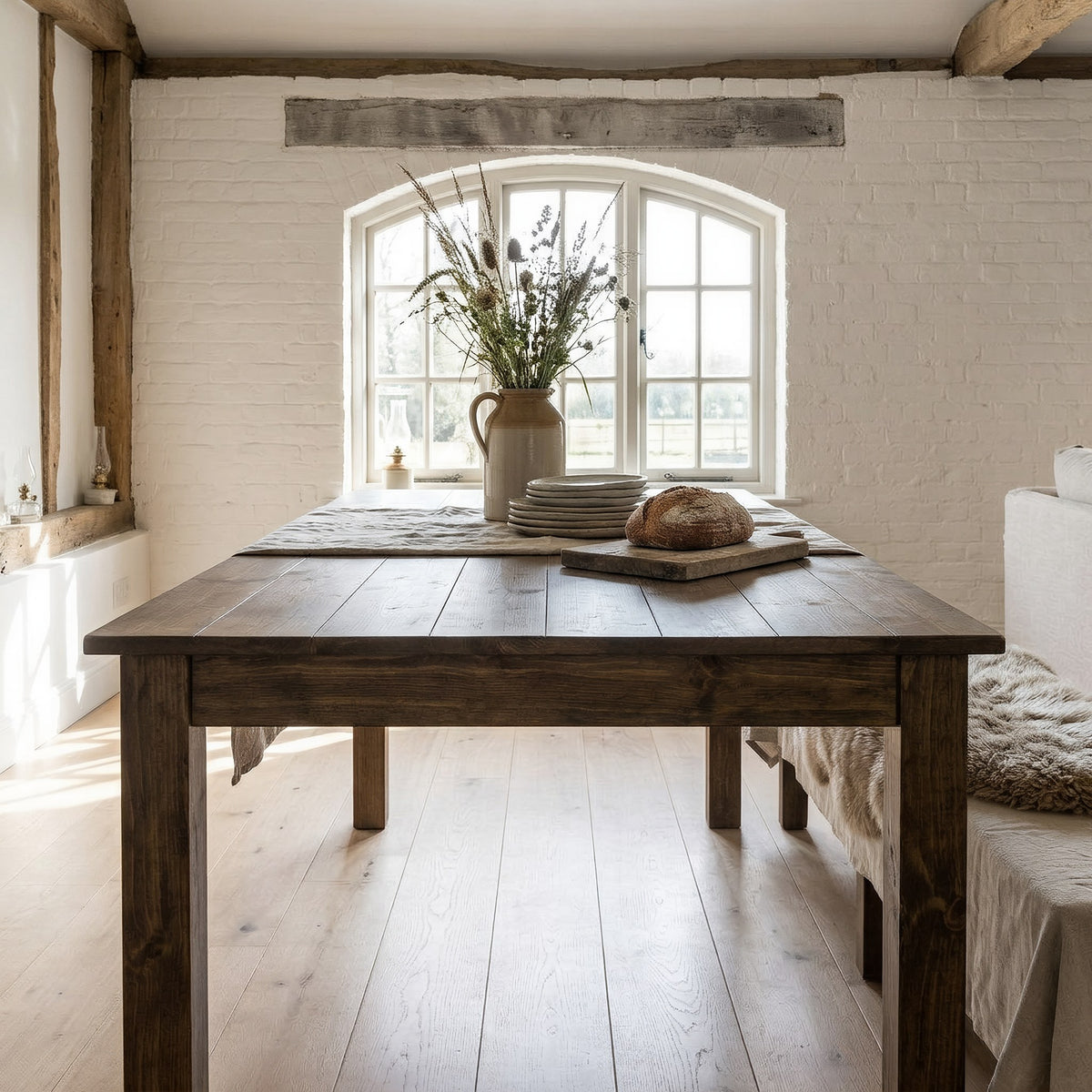 Farmhouse dining table end-on by an arched window in a barn dining hall