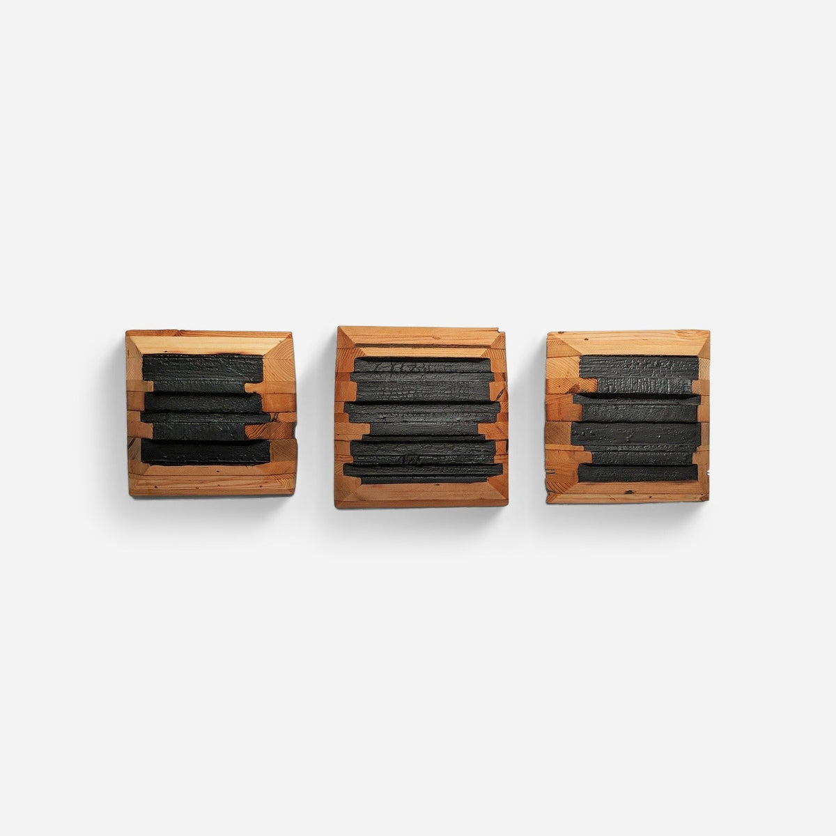 Triptych wood wall art with three black charred panels in oiled wood frames, front view