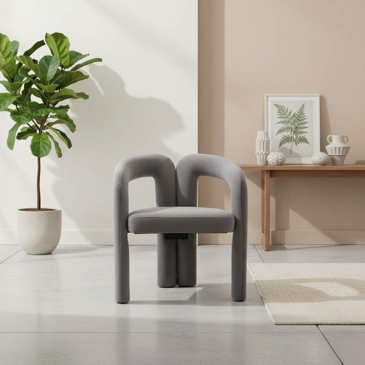 Single gray velvet dining armchair with a curved back in a minimalist room.