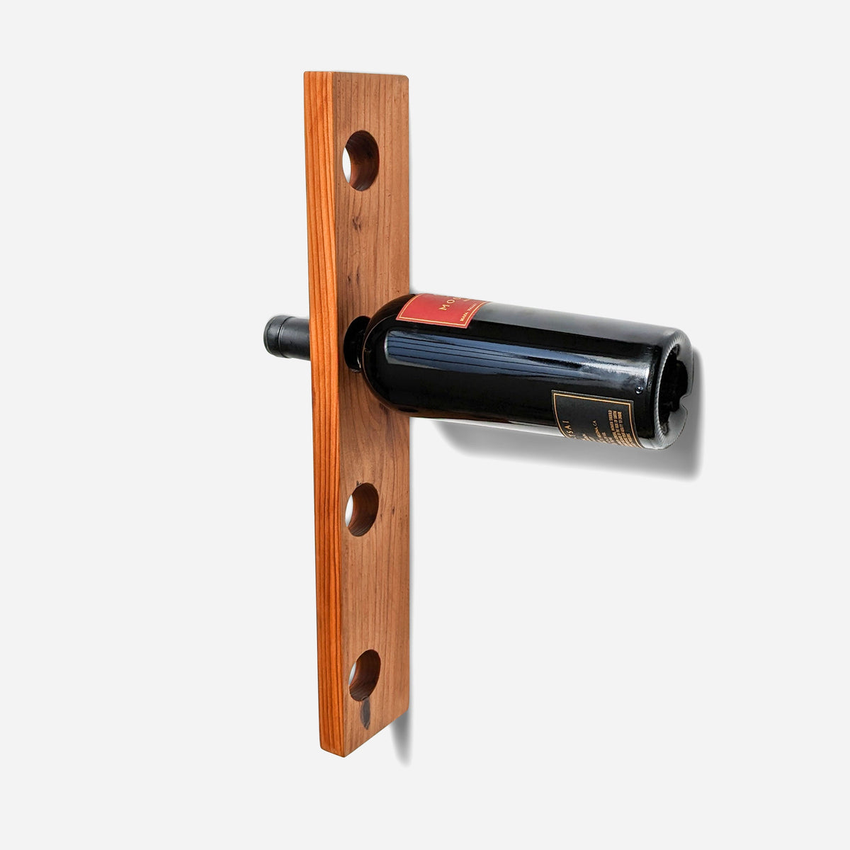 Wall mounted bottle rack in reclaimed fir with four bored holes, holding one dark bottle by its neck