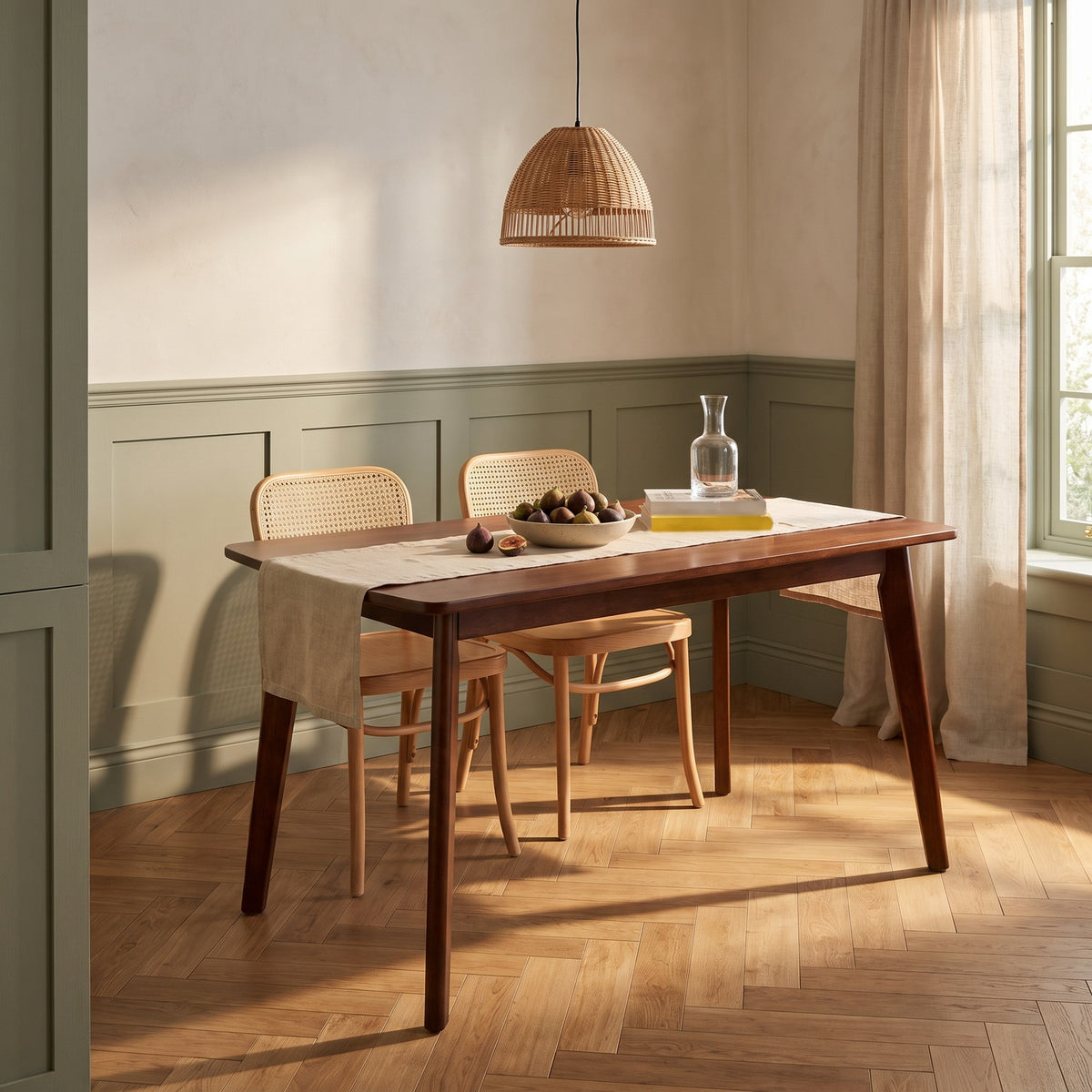 Walnut-finish table in a breakfast room with a sage wainscot, cane chairs and a bowl of figs in late sun