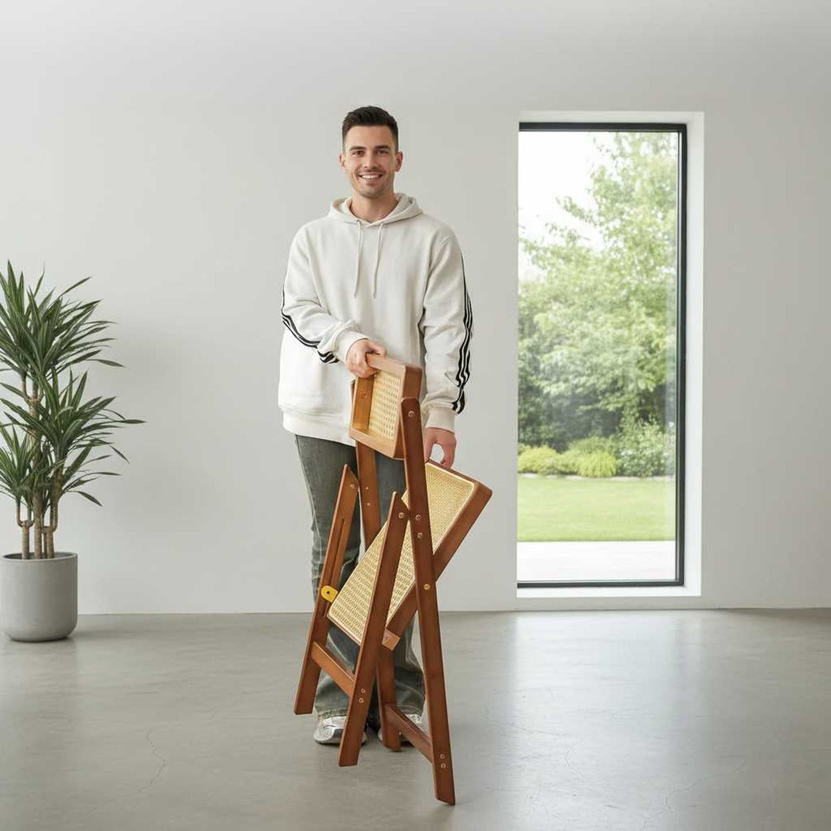 Man holding a walnut-finish rattan folding chair with a woven cane seat indoors.