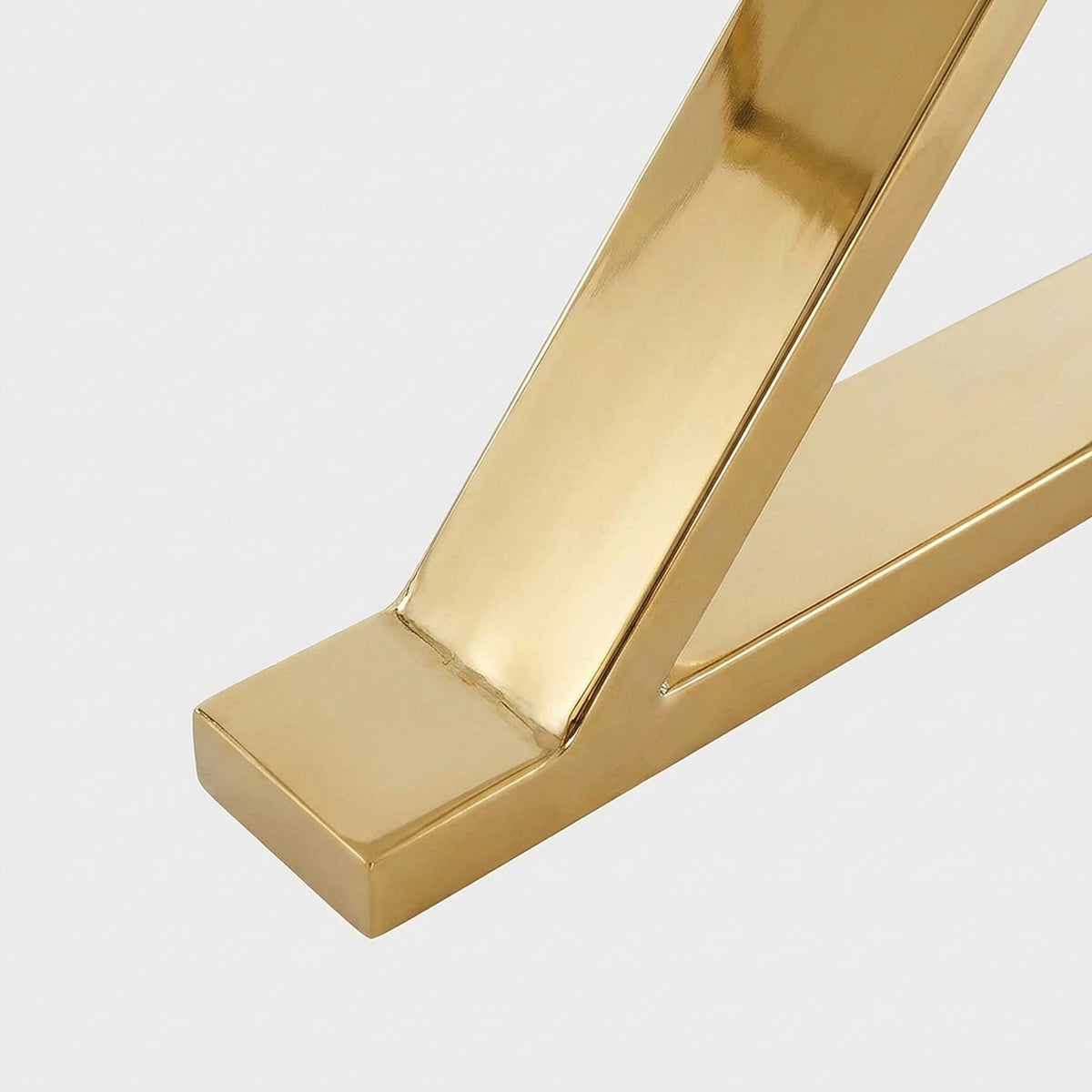 Close-up of the flat gold foot plate under an X leg of the white dining table