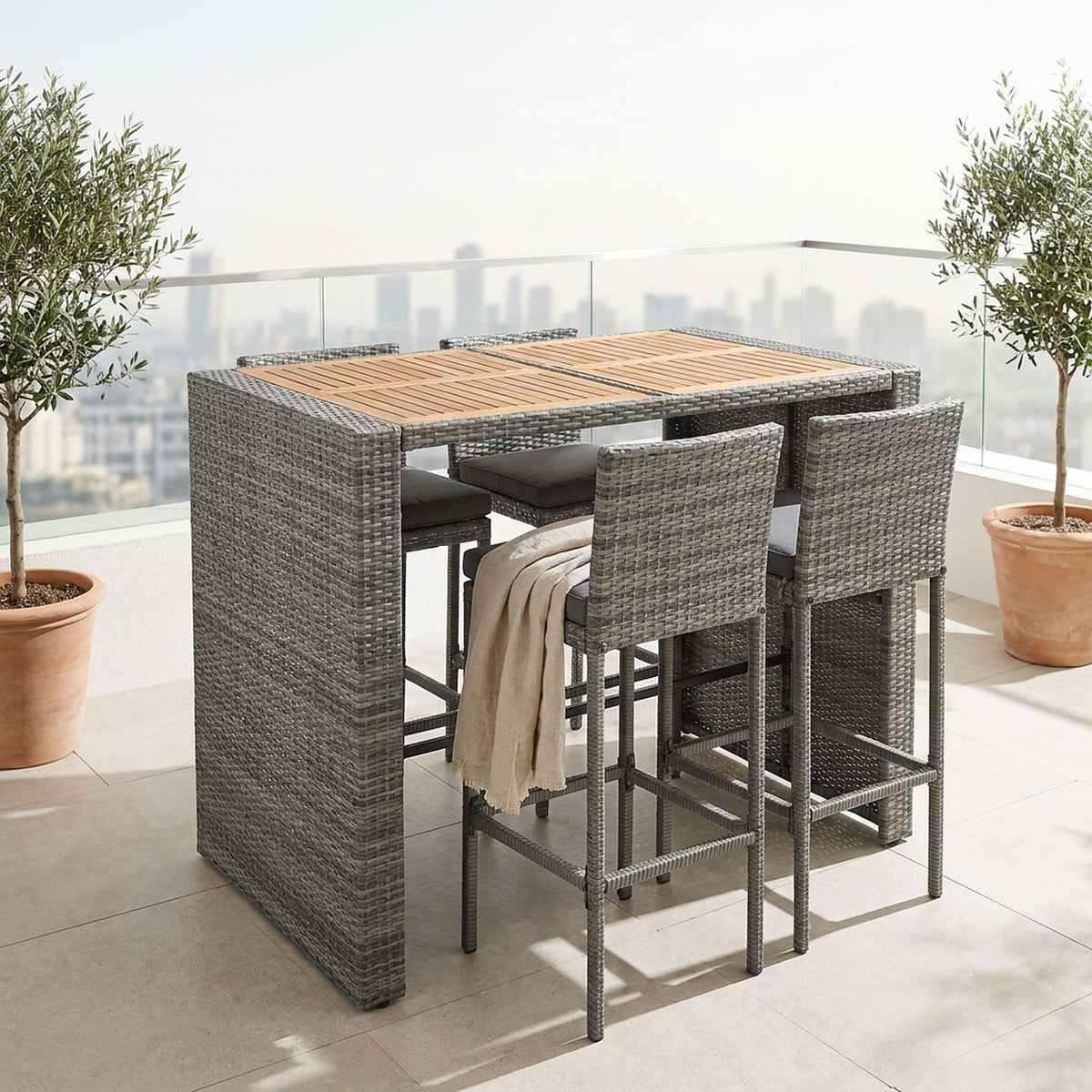Wicker bar table and four stools on a sunlit city rooftop terrace with olive trees