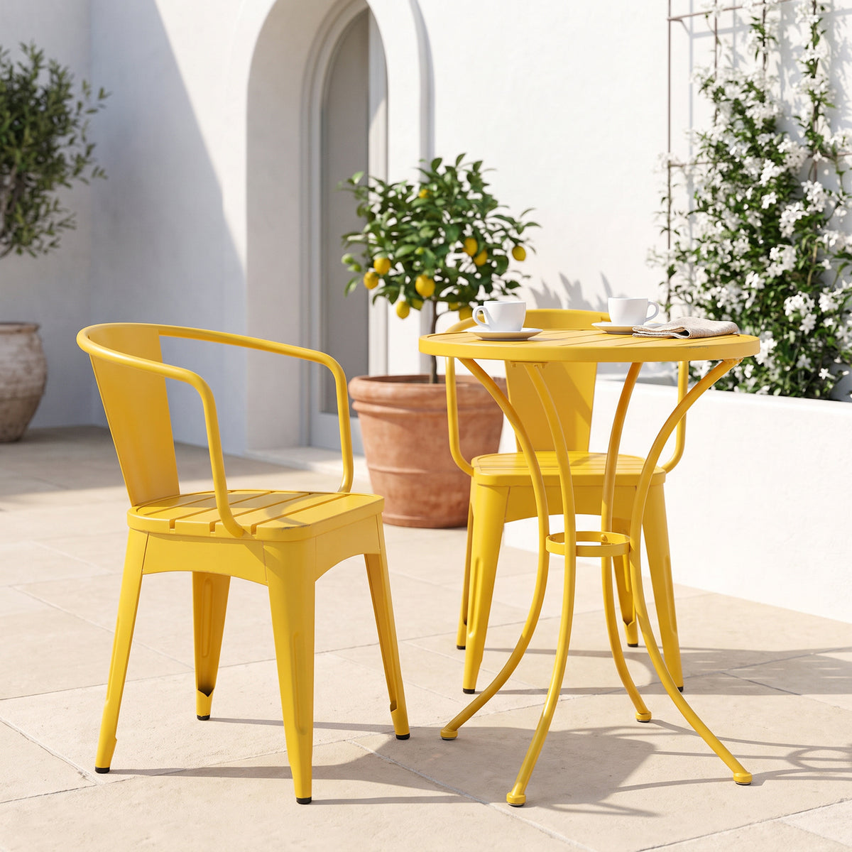 Yellow metal chairs and round table on a pale stone patio with a potted lemon tree and white jasmine